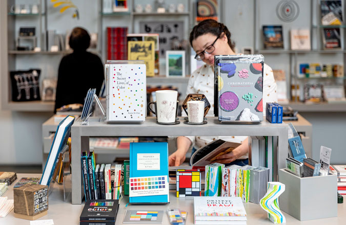 A visitor looks at items, including several books, arranged on a table in the gift shop.