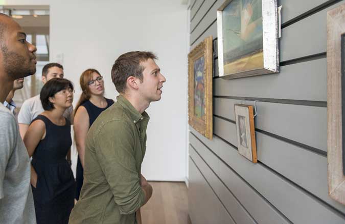 A young man in a green shirt looks closely at a framed object temporarily mounted on a study center wall.