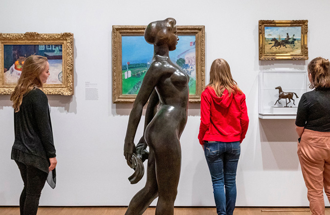 Visitors look at paintings behind a bronze statue of a nude female figure.