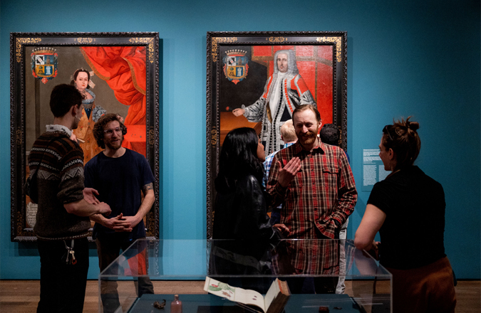 A group of five people in a gallery with large portraits having a conversation.